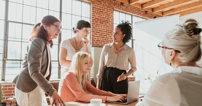 A group of businesspeople talk around a laptop on a table